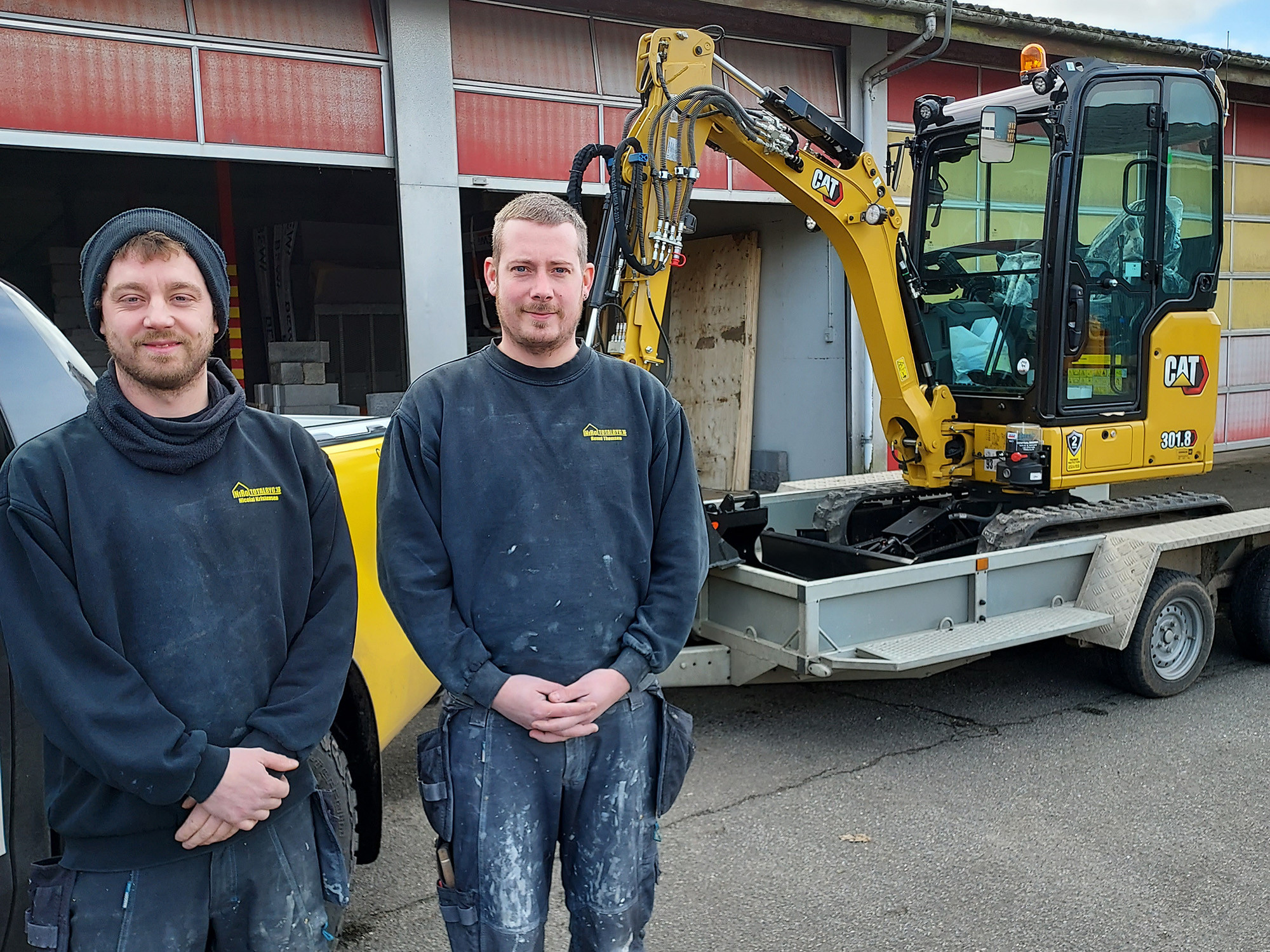 Ronni-Thomsen-og-Nicolai-Kristensen-foran-firmaets-nye-Cat-301.8-gravemaskine-med-forlaenget-gravestick